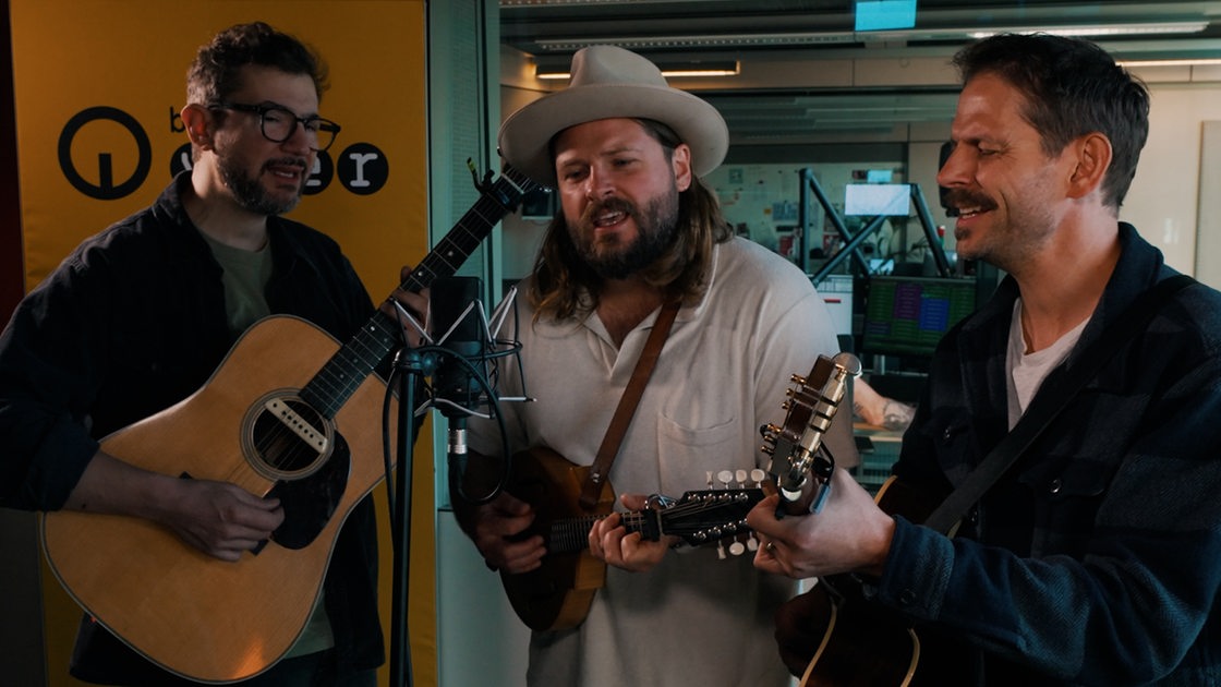 Drei Männer spielen Akustik-Gitarre und singen