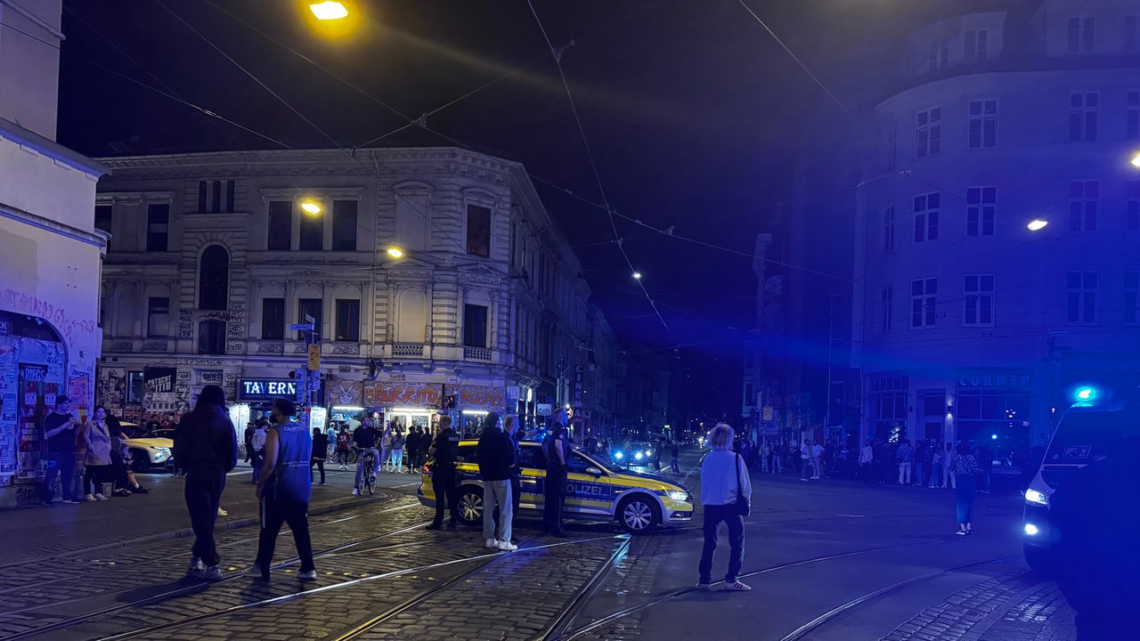 Ein Polizeiauto steht in der Nacht auf einer Kreuzung im Bremer Viertel. Menschen laufen drumherum.